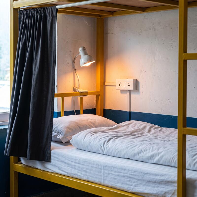 A single bunk with the curtain half open, showing the clip lamp and the socket at pillow height