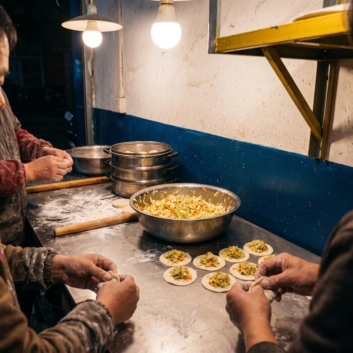 Hands folding momos on a steel table in the hostel kitchen