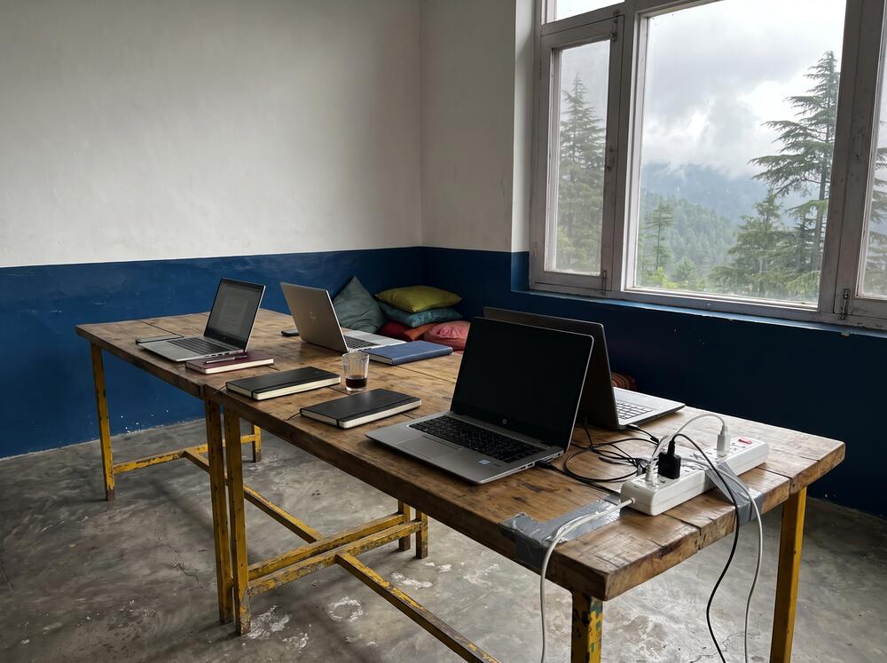 The work corner of the common room, long shared table with laptops and a view down the valley
